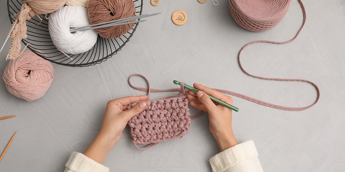 Woman crocheting with threads at grey table, top view. Engaging